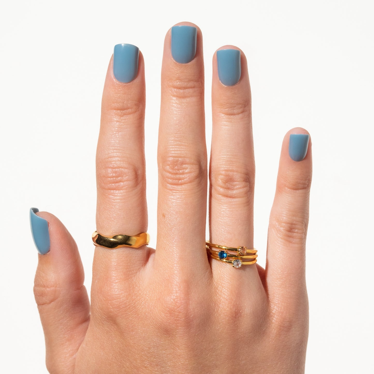 Hand with gold rings and blue press on nails on a white background