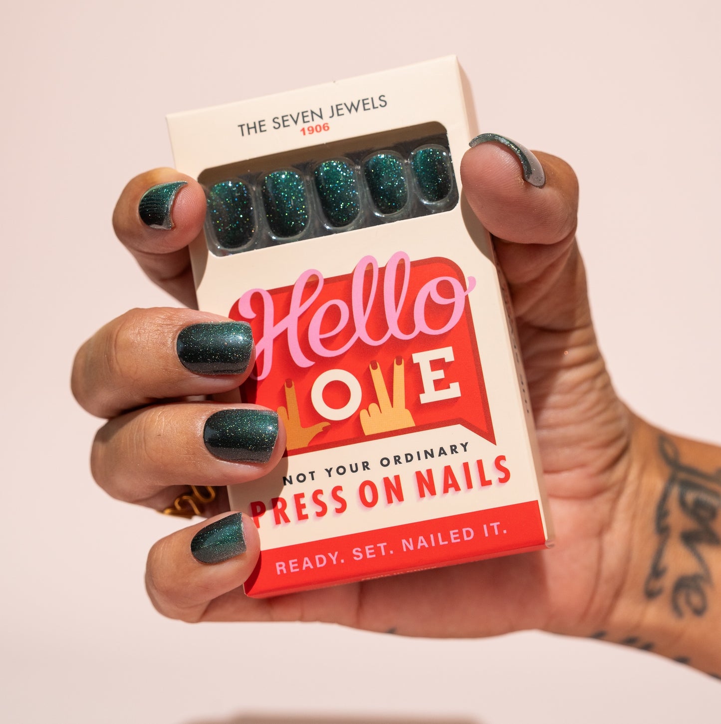 Hand holding a box of press-on nails with a visible brand name on a light pink background