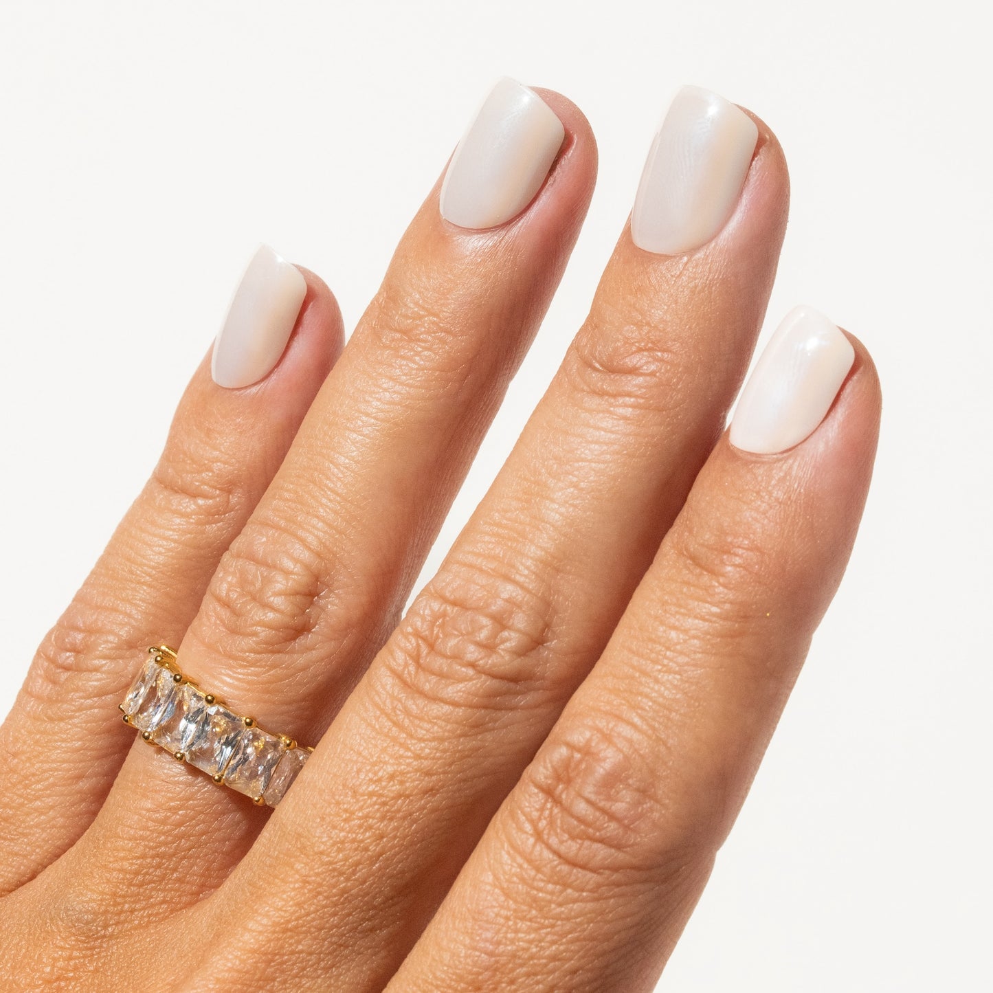 Hand wearing off white press on nails with a gold ring on a white background