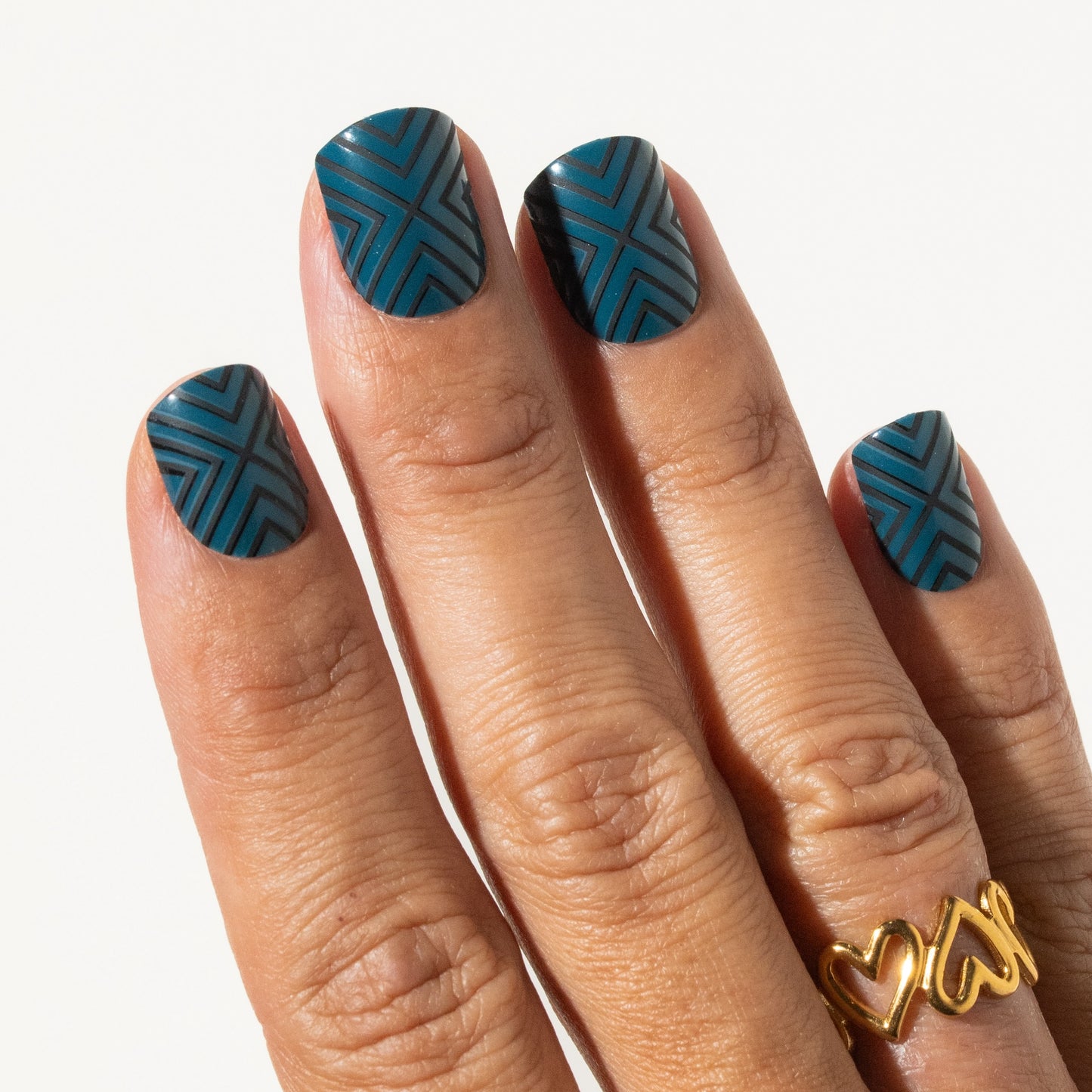 Hand with teal press on nails and a gold ring on a white background