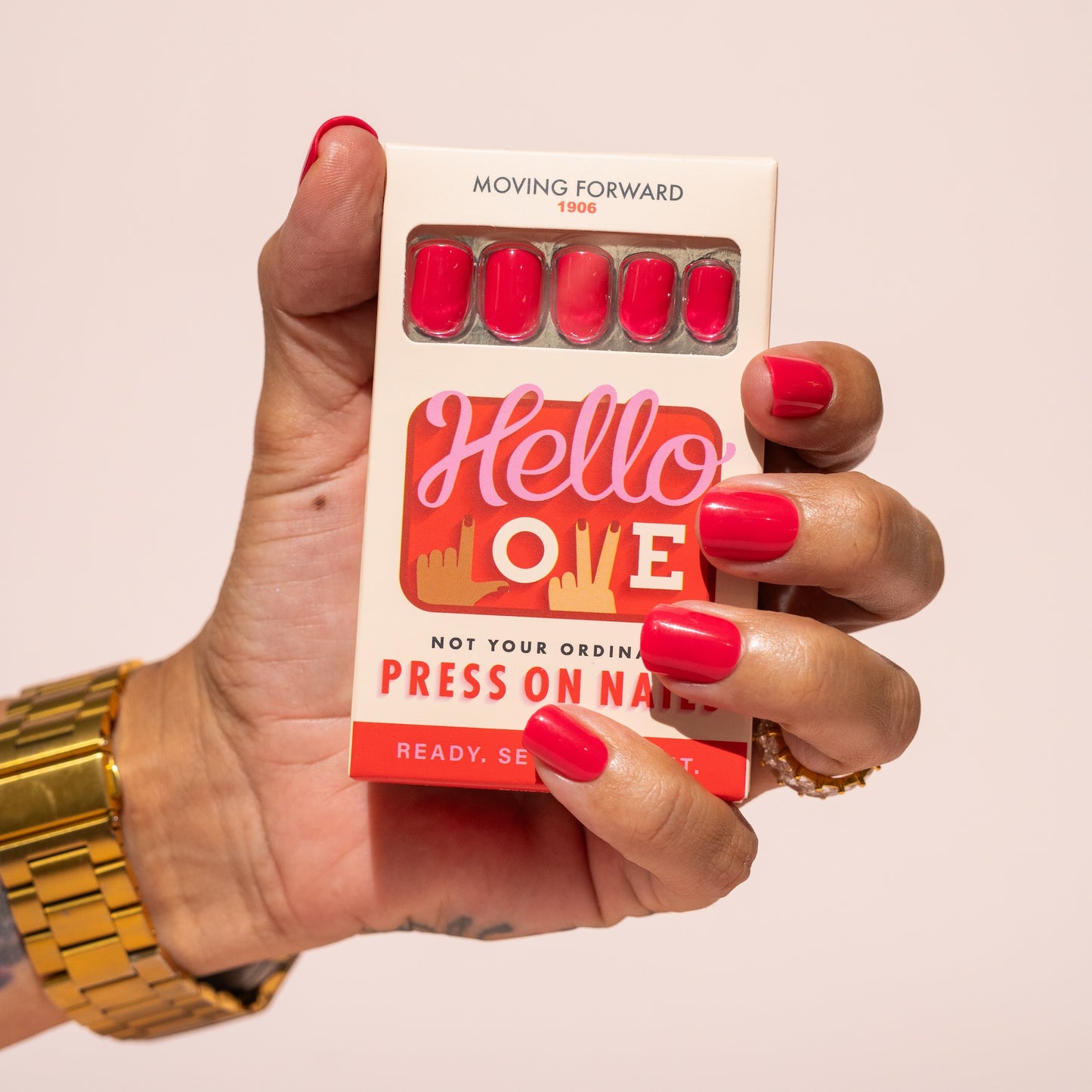 Hand holding a box of press-on nails with pink red nails and 'Hello Love' branding.