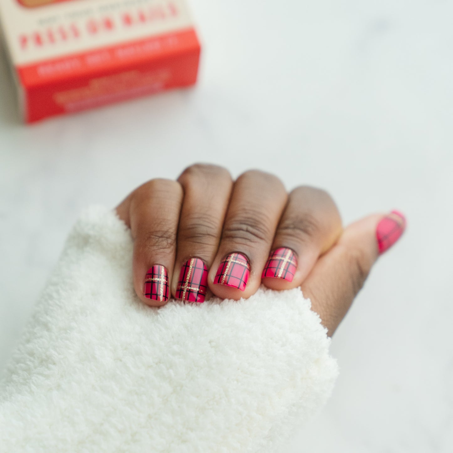 Hand with red and black plaid nail design on a white background