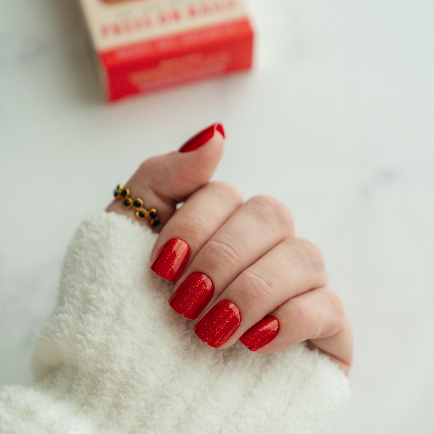 Hand with red nail polish on a white surface
