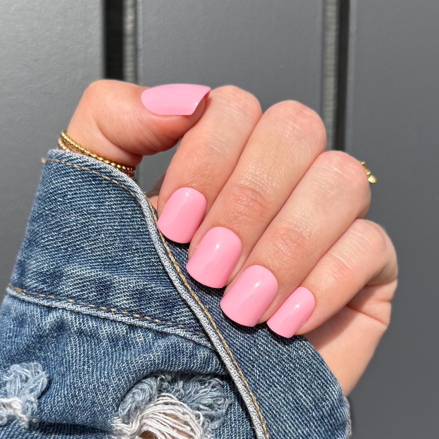 Hand with pink nails wearing a denim jacket against a gray background
