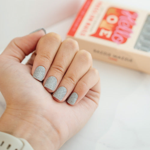 Hand with silver glittery press on nails holding a small box.