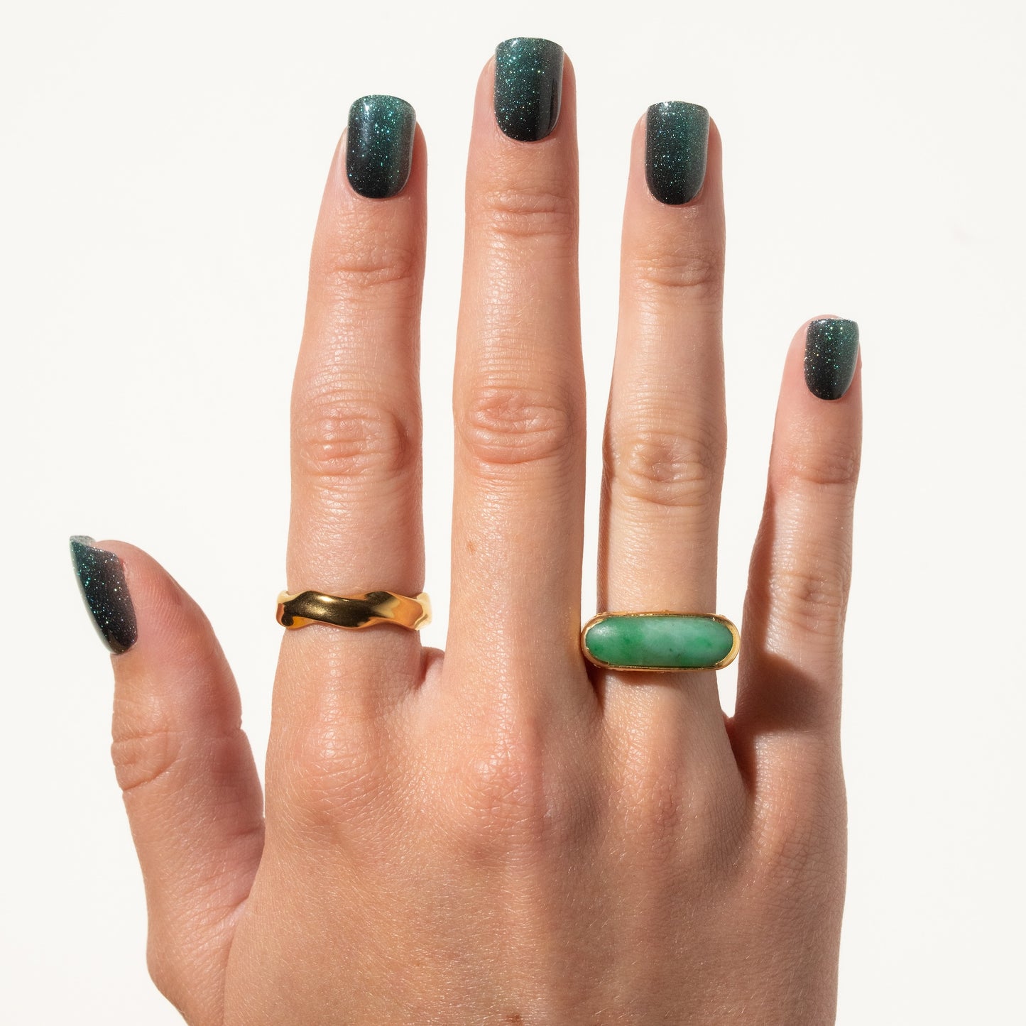 Hand wearing two rings with green press on nails on a white background