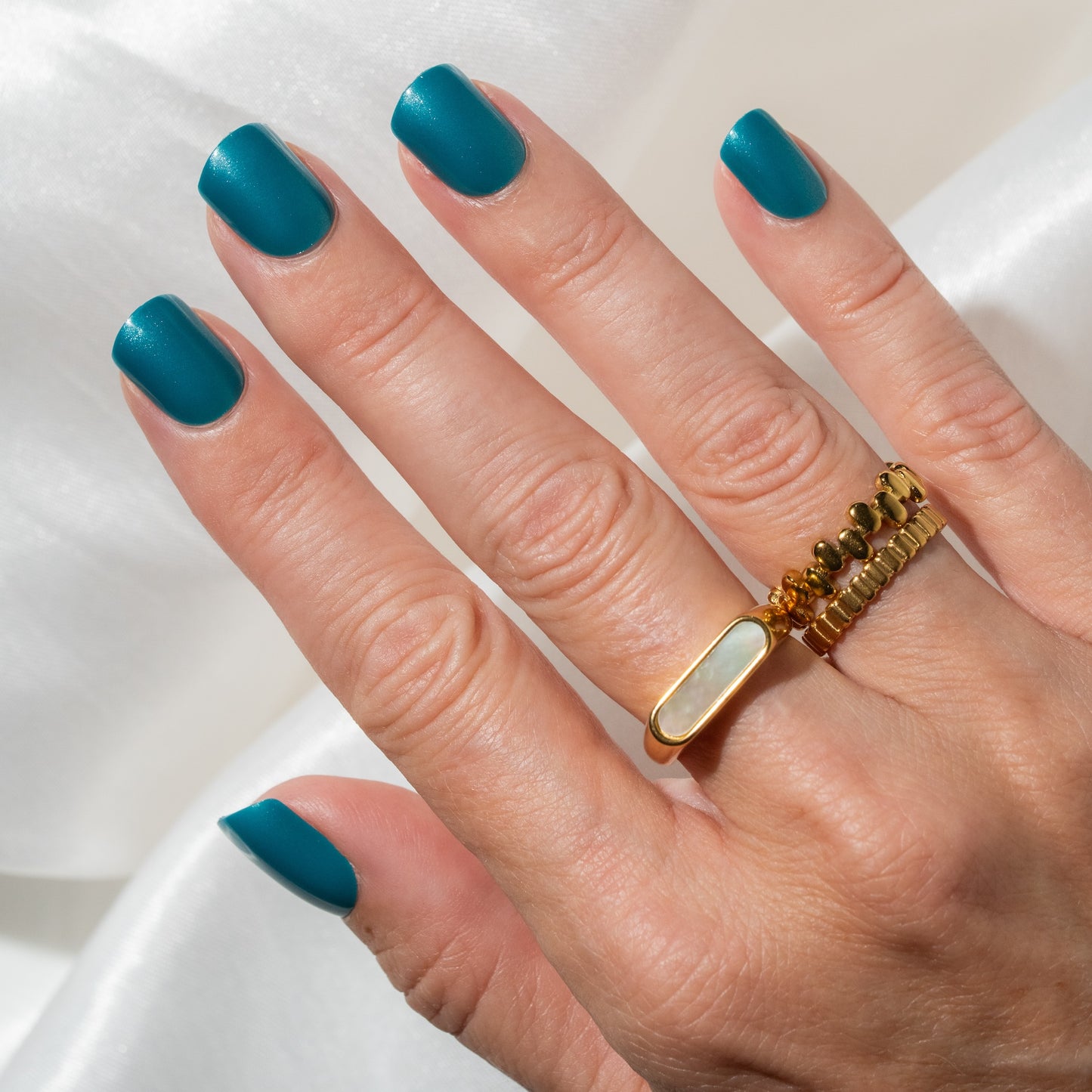 Hand with teal press on nails wearing a gold ring on a white background