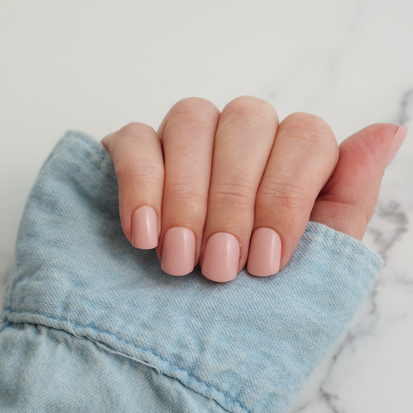 Hand with light pink press on nails holding a denim fabric