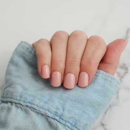 Hand with light pink press on nails holding a denim fabric