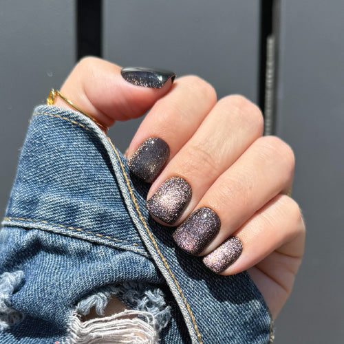 Hand with glittery press on nails holding a denim jacket against a gray background