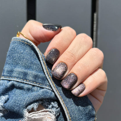Hand with glittery press on nails holding a denim jacket against a gray background