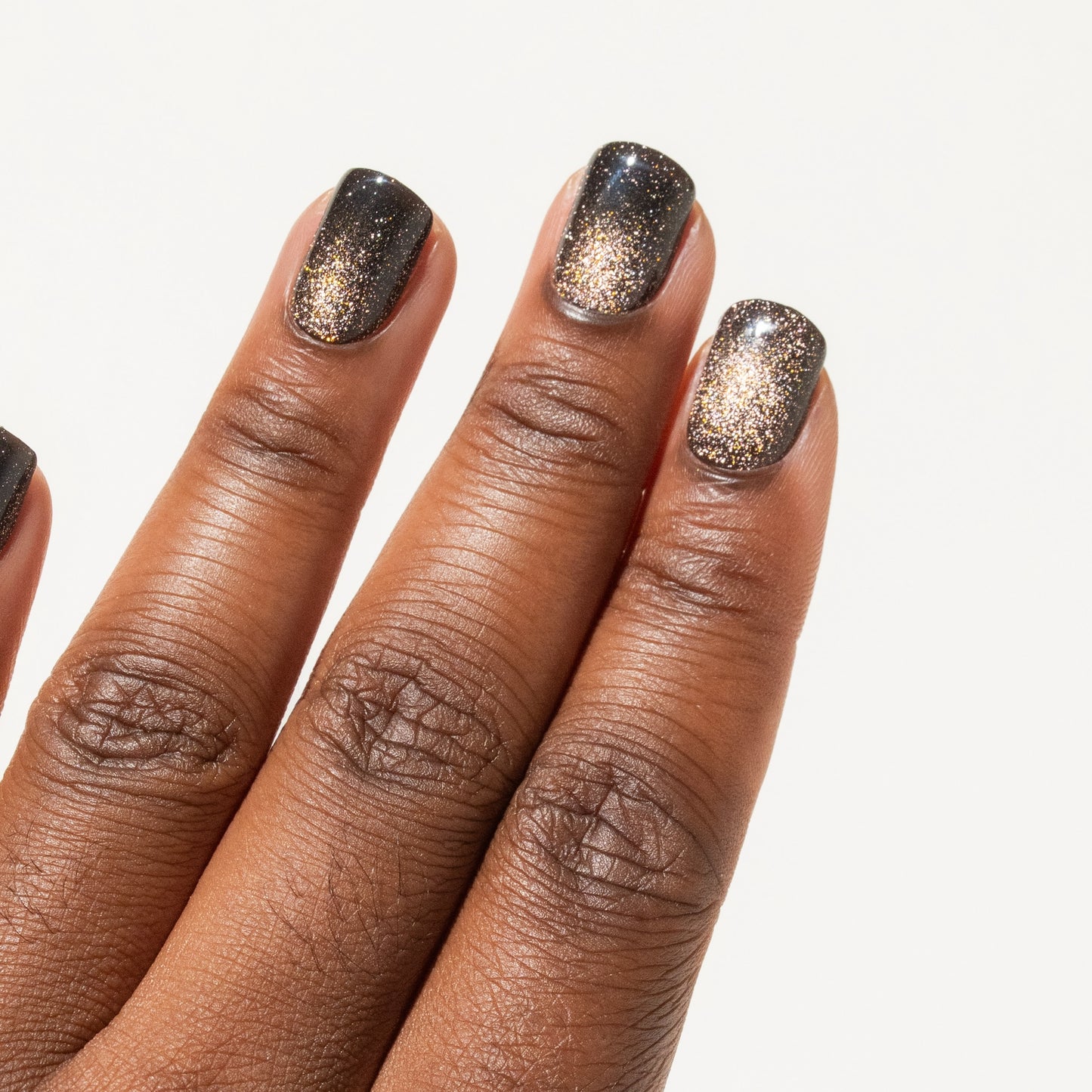 Close-up of a hand with glittery black press on nails on a white background