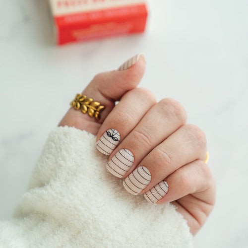 Hand with striped press on nails wearing a gold ring on a white background
