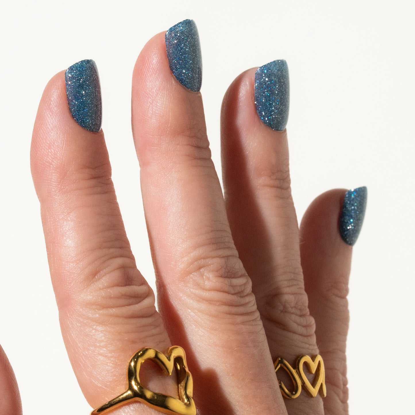 Close-up of a hand with blue glittery press on nails on a white background