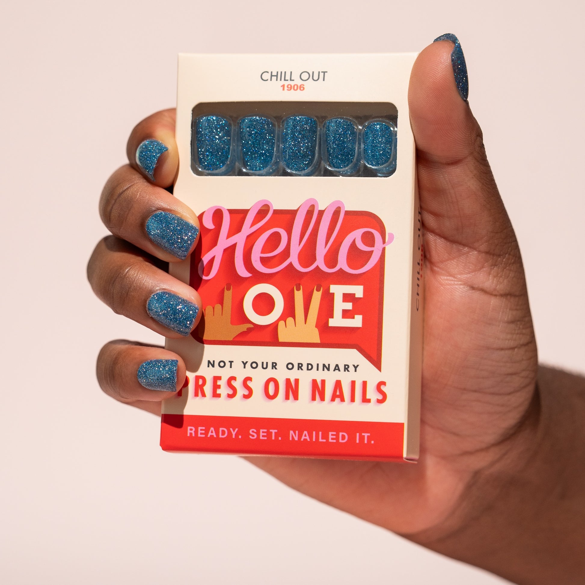 Hand holding a box of press-on nails with 'Hello Love' branding.