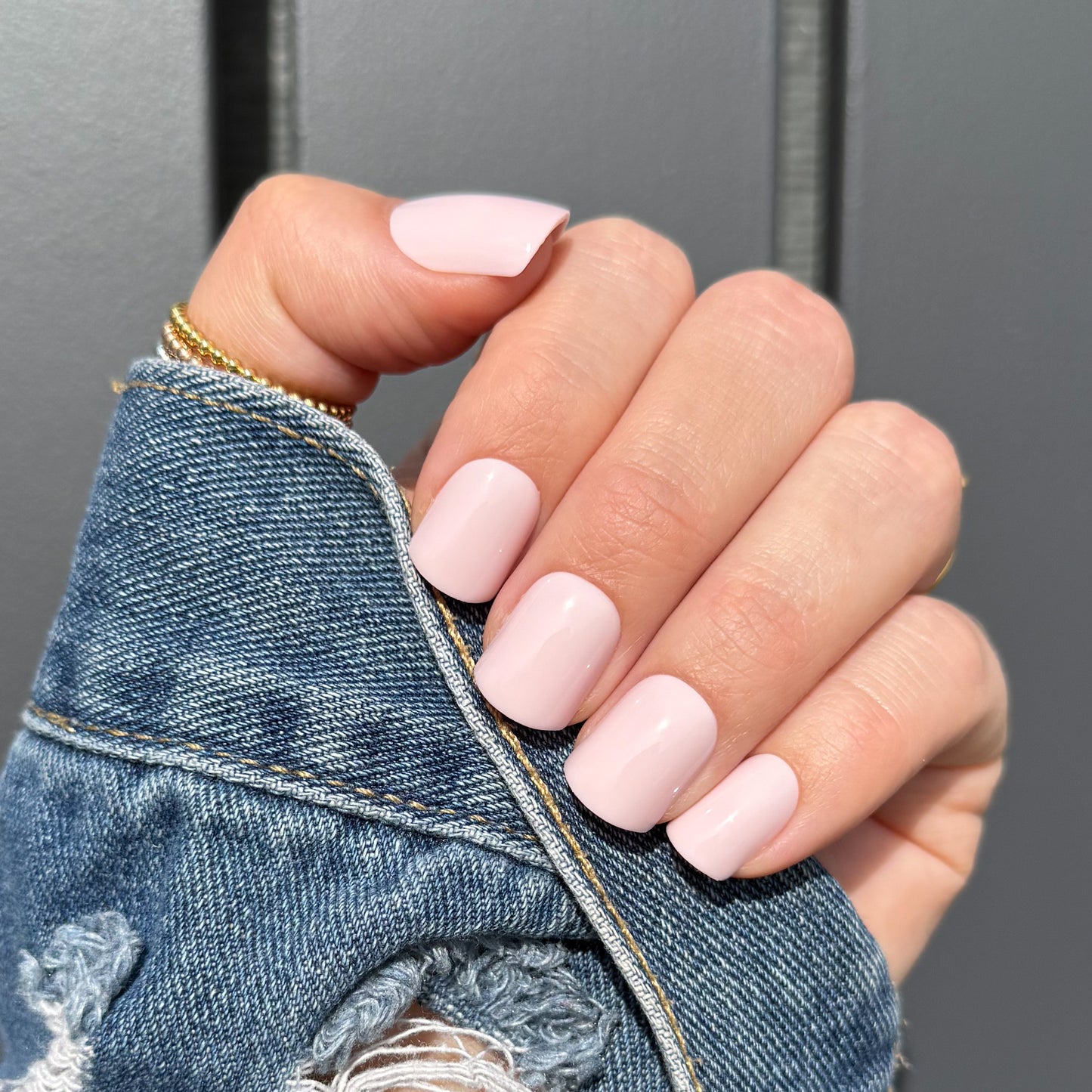 Hand with pink press on nails wearing a denim jacket against a gray background