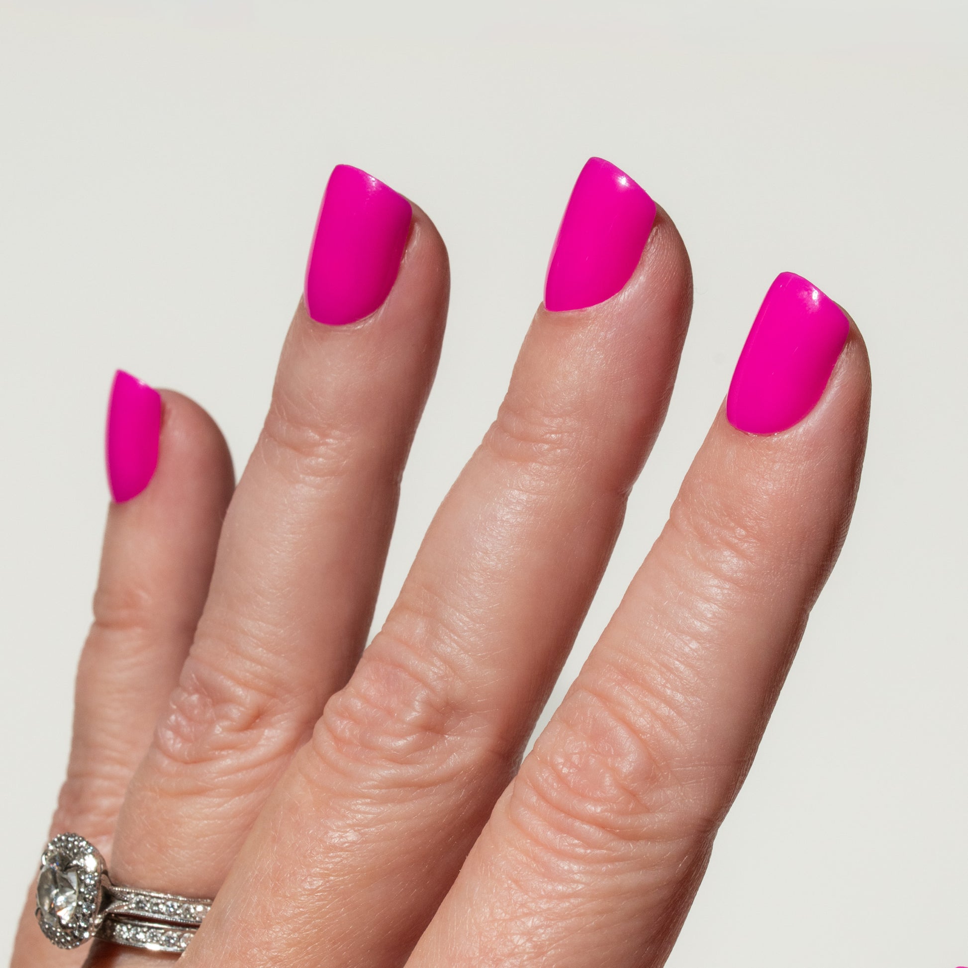 Hand with bright pink nails on a plain background