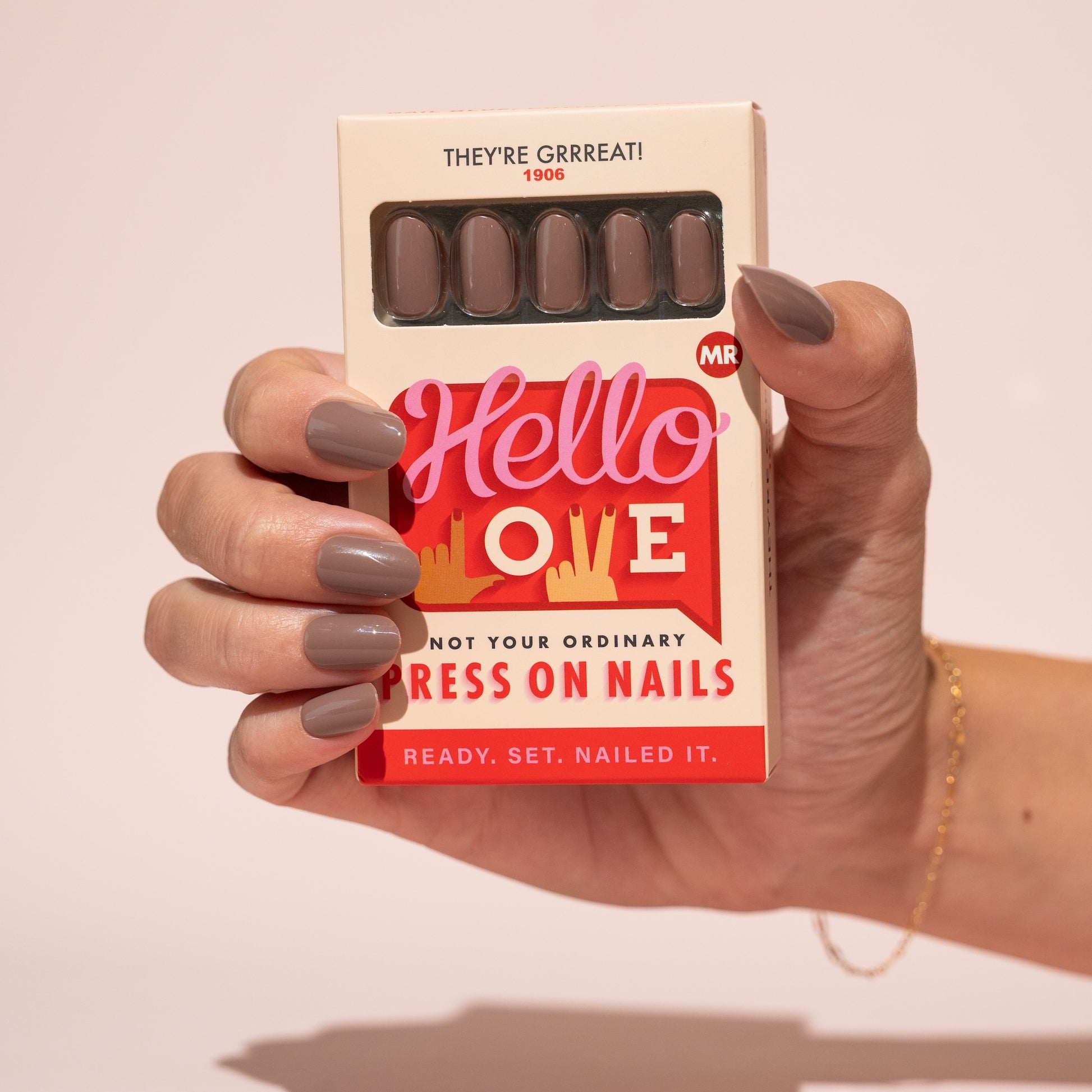 Hand holding a box of brown press-on nails with a pink background