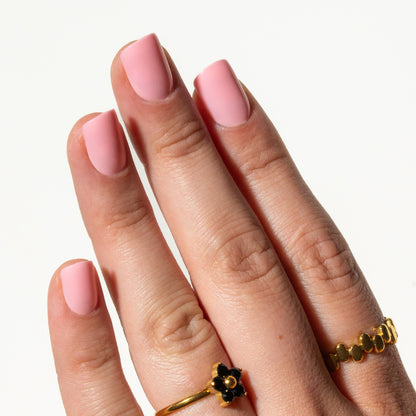 Hand with pink nails wearing two gold rings on a white background