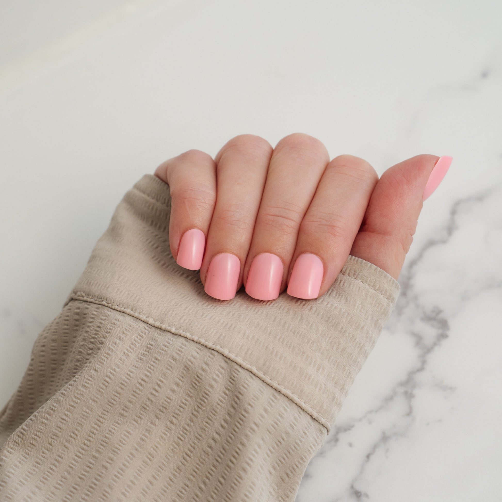 Hand with pink press on nails on a marble surface