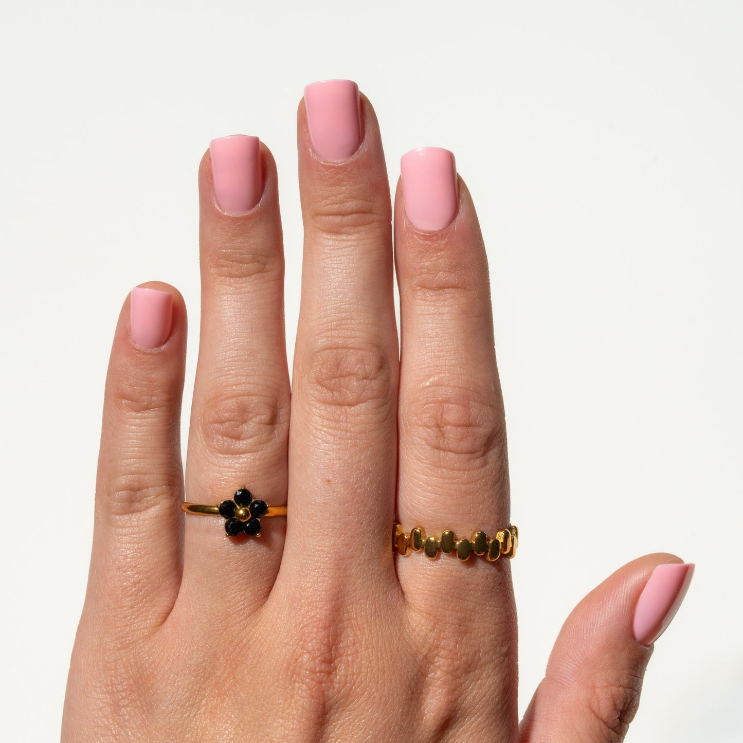 Hand wearing two gold rings with pink press on nails on a light background