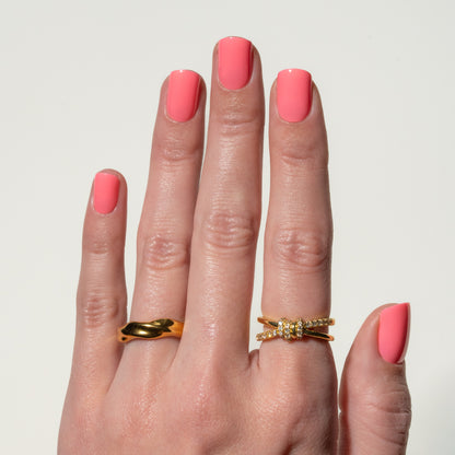 Hand with pink press on nails wearing two gold rings on a light gray background