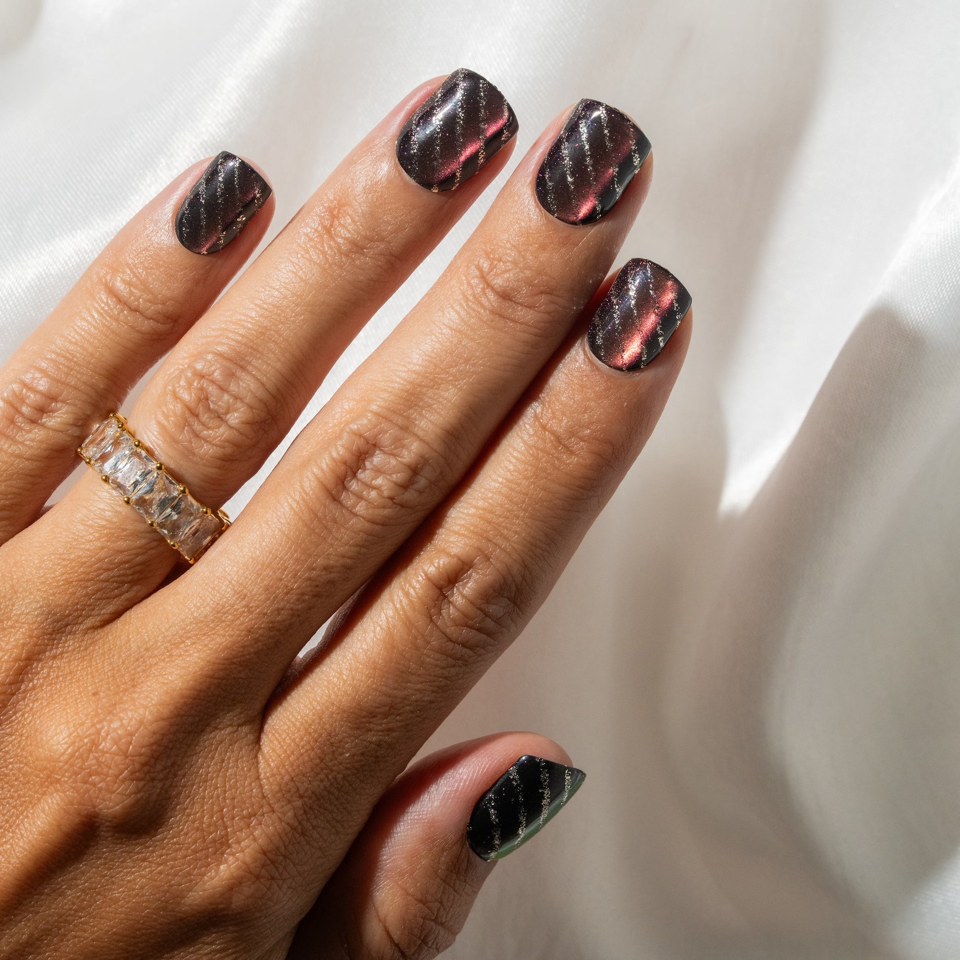 Hand with purple press on nails wearing a gold ring on a white background