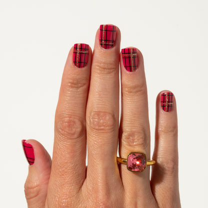 Hand with red Christmas plaid press on nails wearing a gold ring with a pink gemstone on a white background