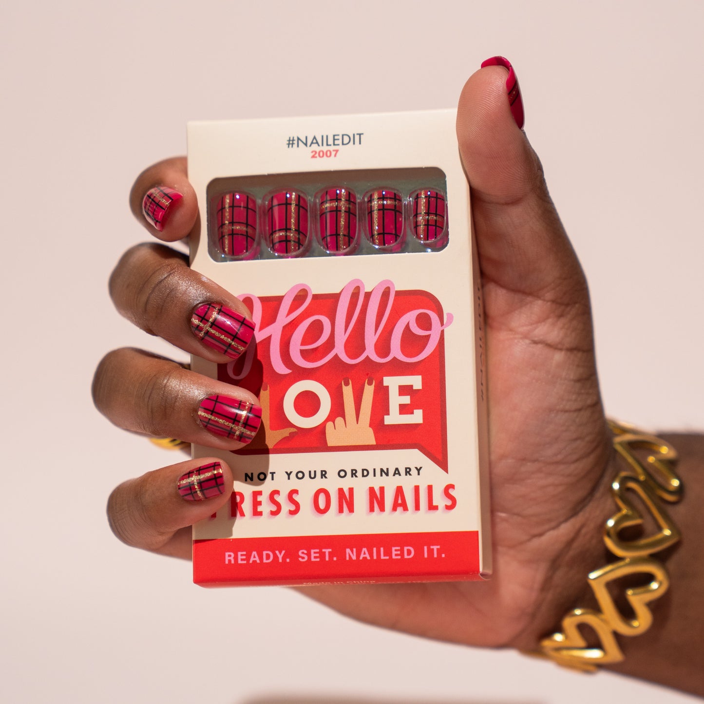 Hand holding a box of press on nails with red Christmas plaid design