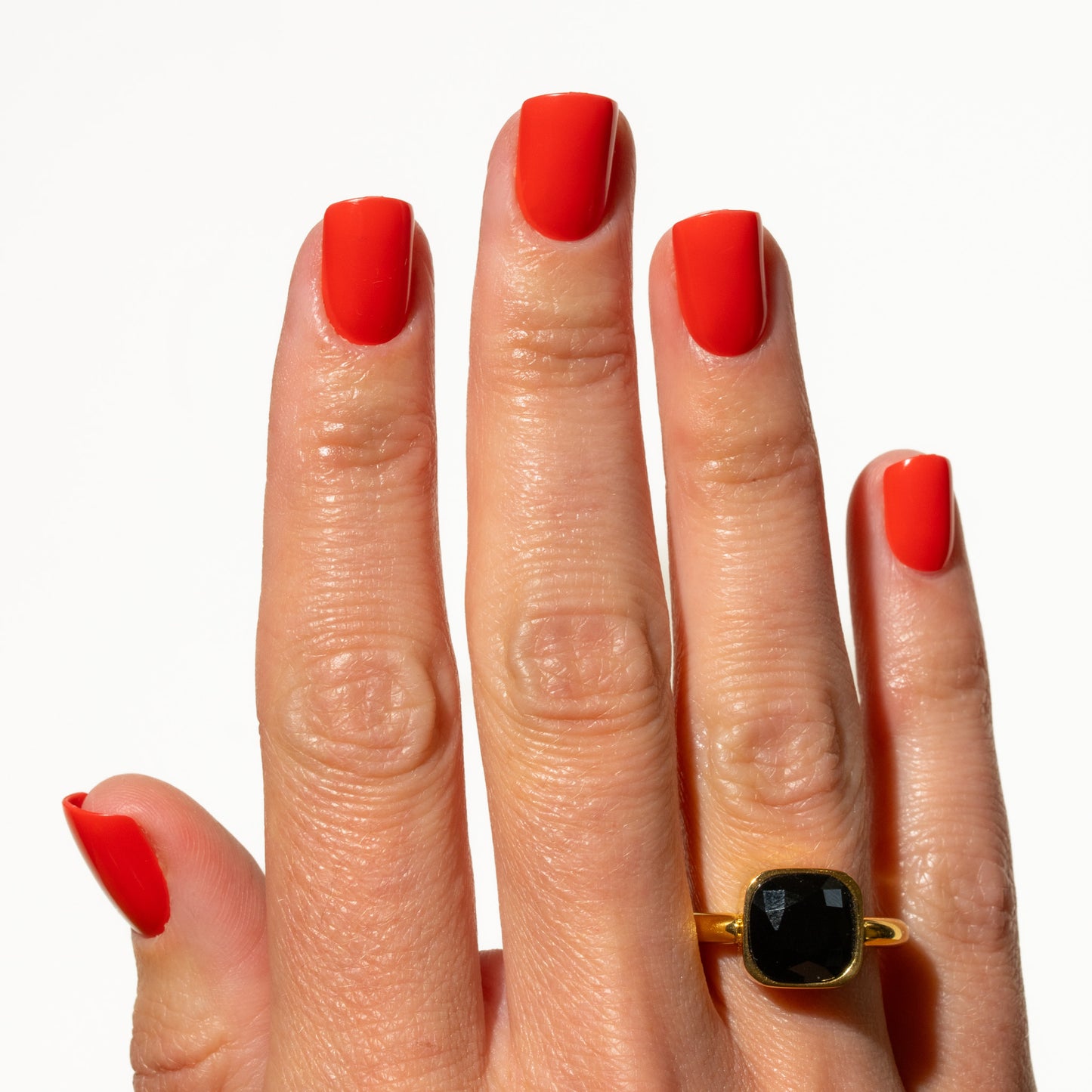 Hand with red press on nails wearing a gold ring with a black gemstone on a white background