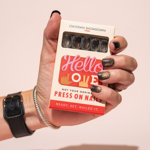 Hand holding a box of press-on nails with 'Hello Love' branding on a light pink background