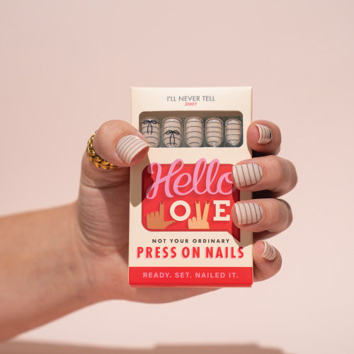 Hand holding a box of press-on nails with a pink background