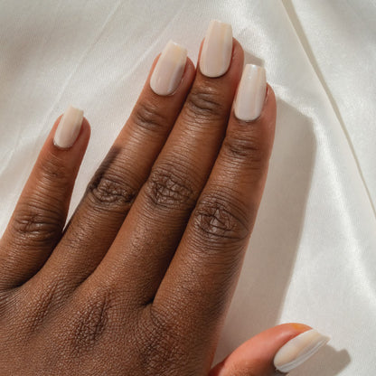 Hand with cream colored press on nails on a white fabric background