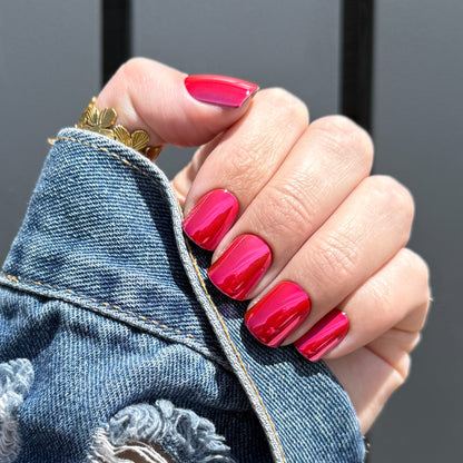 Hand with dark pink press on nails wearing a gold ring, holding denim fabric.