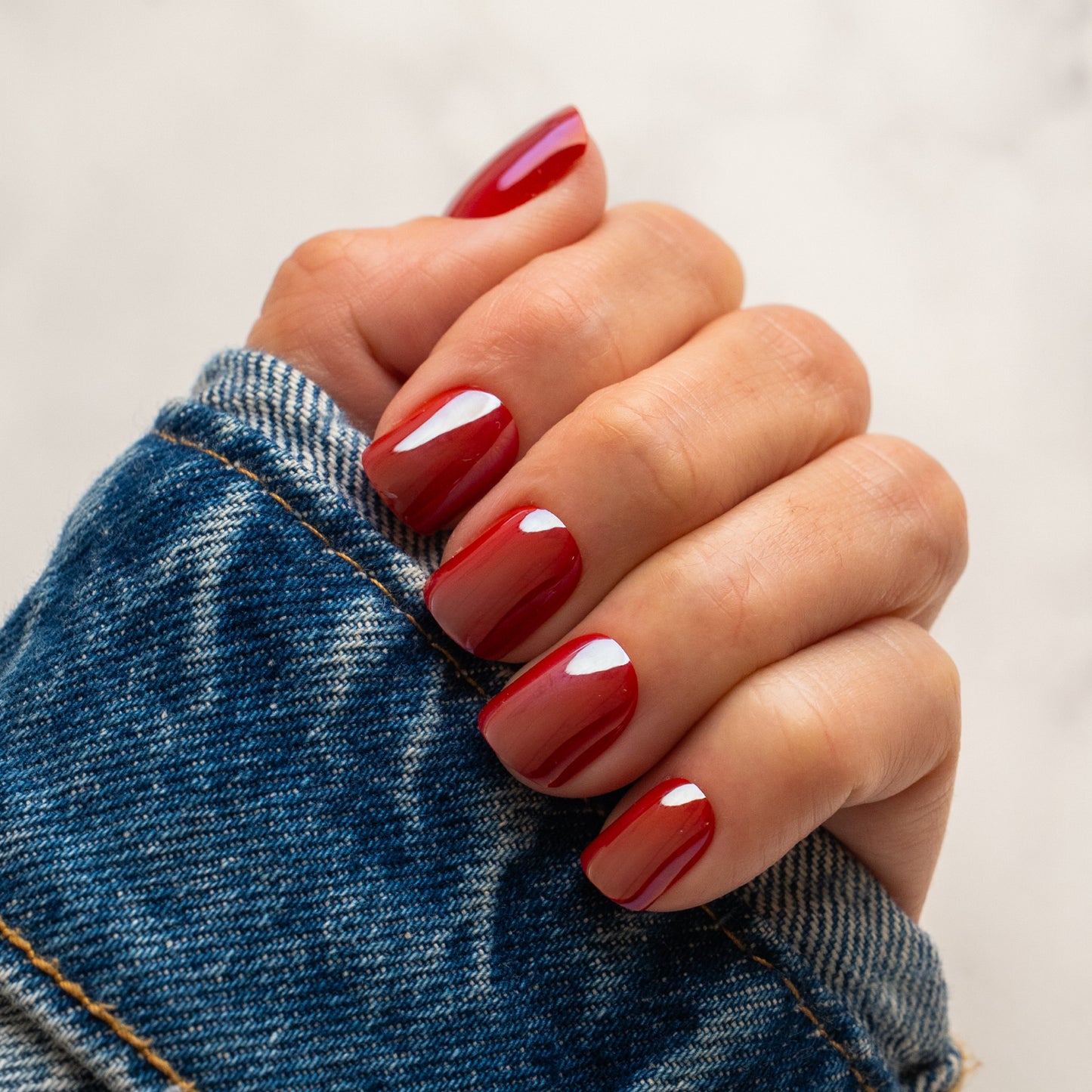 Hand with red press on nails holding a denim jacket against a neutral background