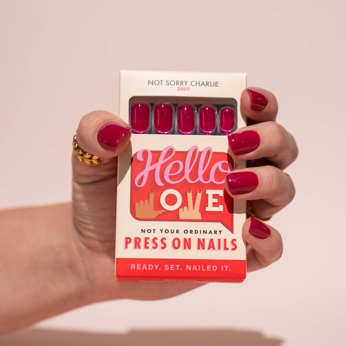 Hand holding a box of press-on nails with berry pink nails and 'Hello Love' branding.