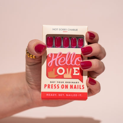 Hand holding a box of press-on nails with berry pink nails and 'Hello Love' branding.