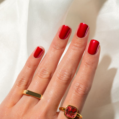 Hand with bright pink press on nails wearing two gold rings on a white background