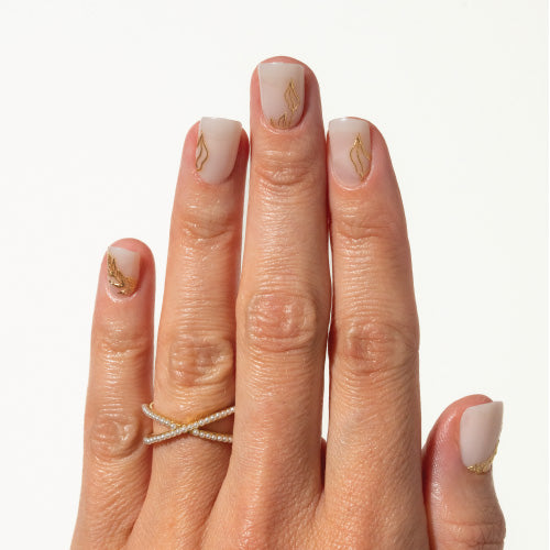 Hand with milky white press on nails and gold leaf designs, wearing a gold ring on a white background