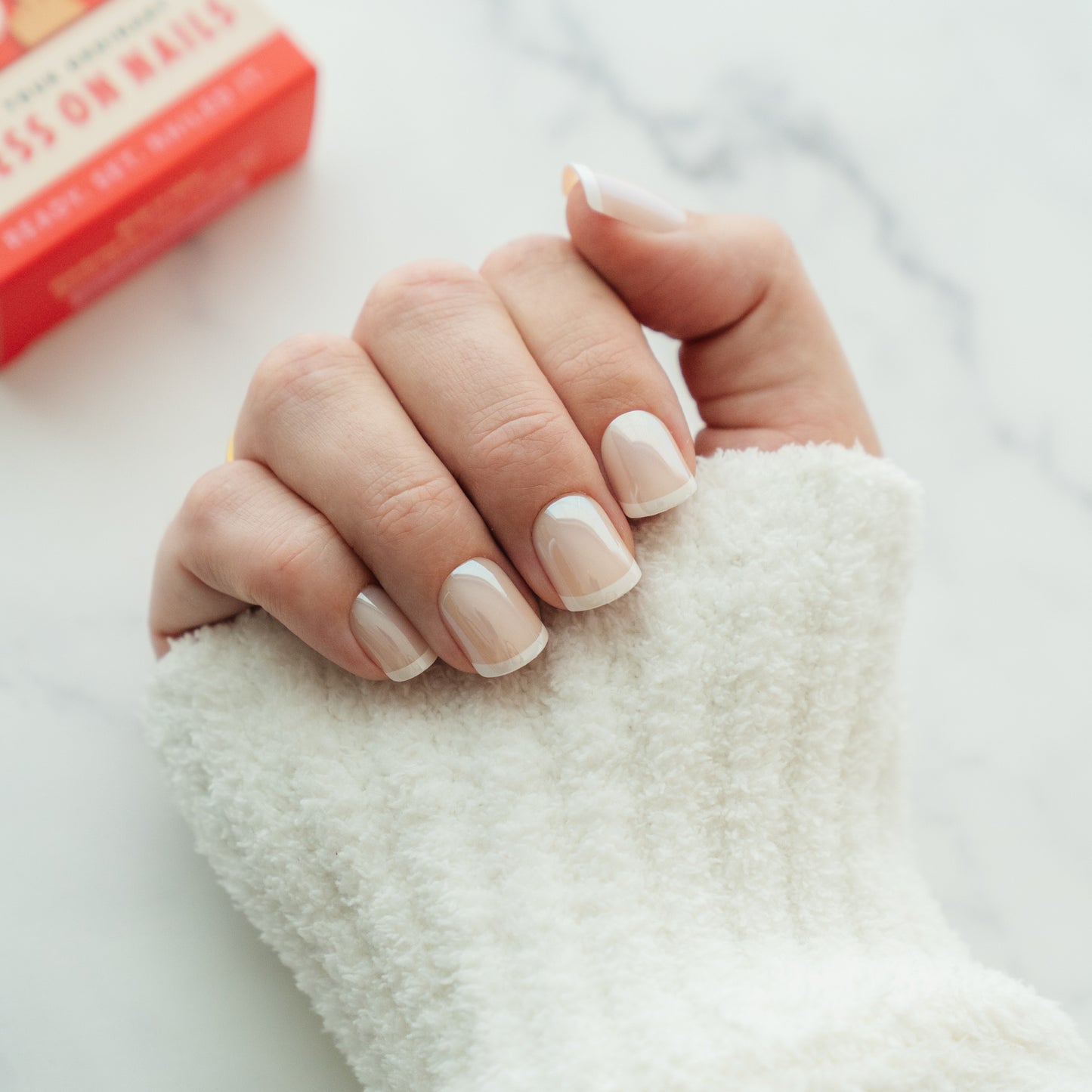 Hand with french manicure press on nails  with a red box in the background.
