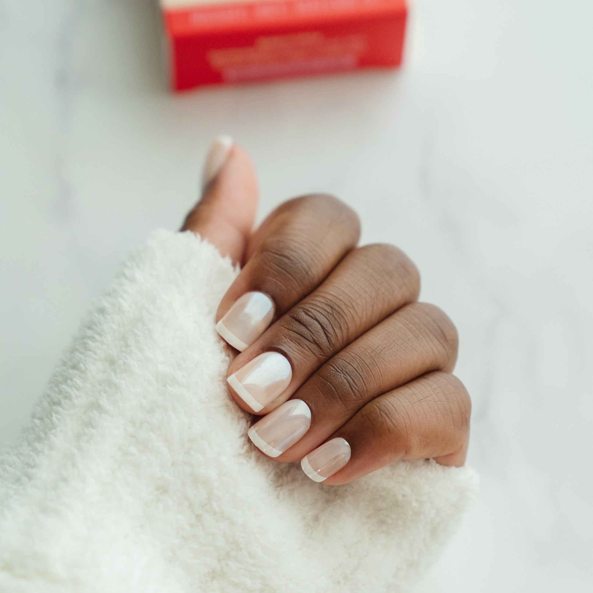 Hand with french manicure press on nails, with a red box in the background.