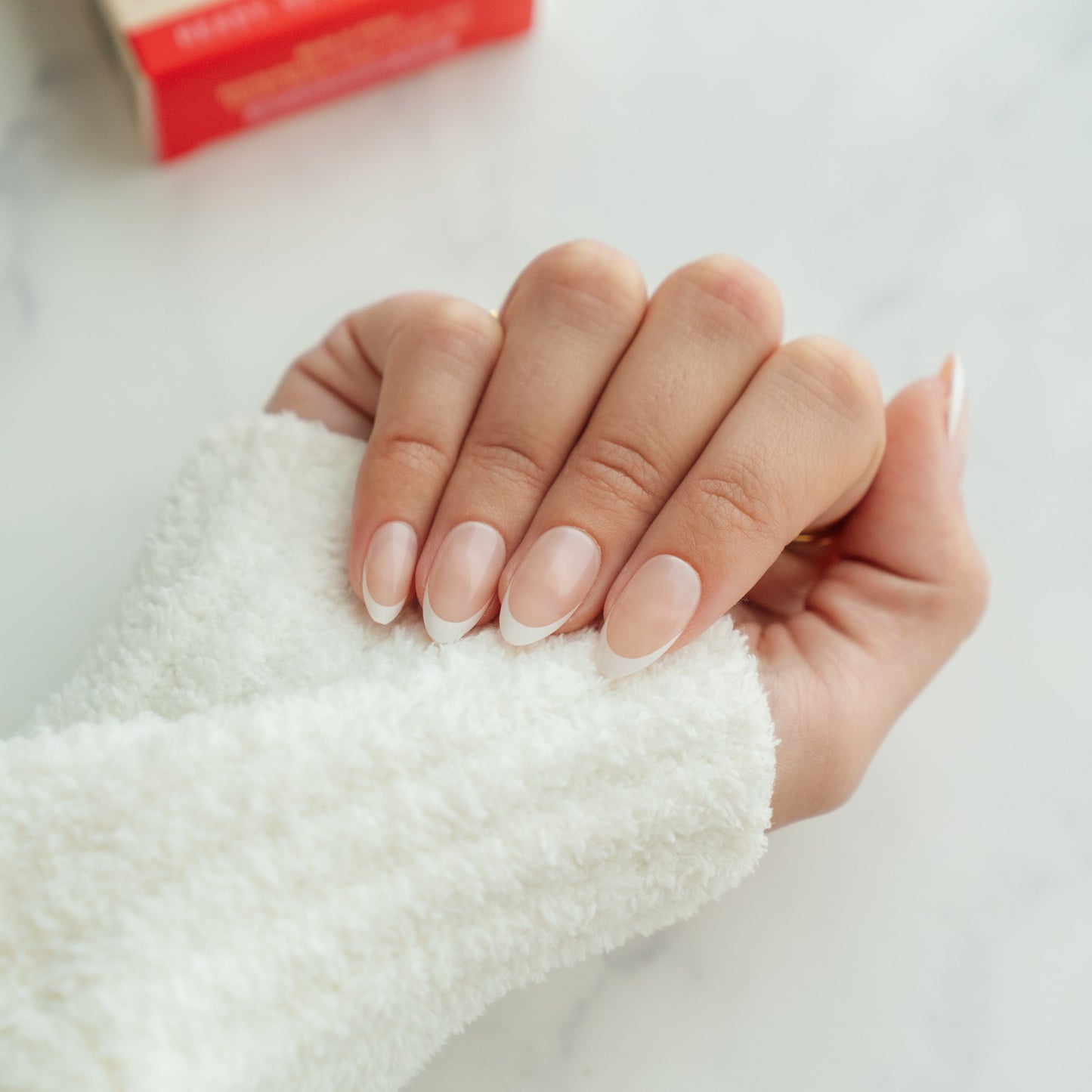 Hand with neatly manicured nails holding a white towel on a light background