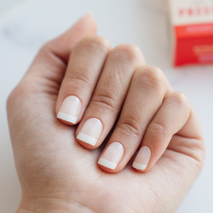 Close-up of a hand with light pink nail polish on a neutral background
