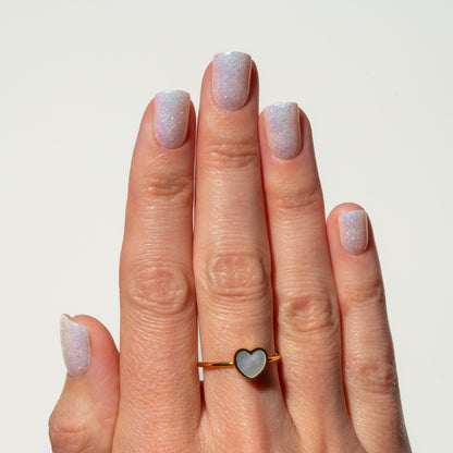 Hand with glittery nails wearing a heart-shaped ring on a plain background