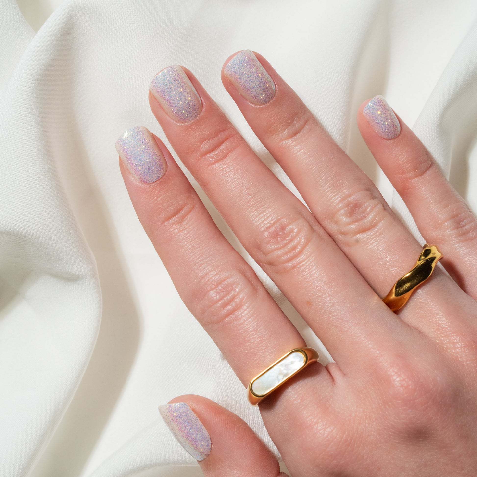 Hand wearing a gold ring with a white stone on a light background