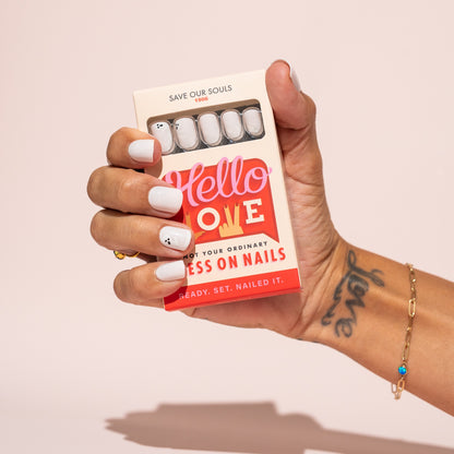 Hand holding a box of 'Hello Love' Halloween press on nails with a pink background
