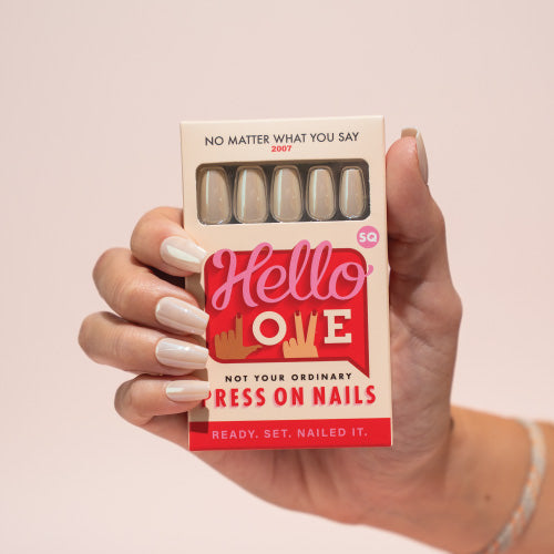 Hand holding a box of press-on nails with 'Hello Love' branding on a light pink background