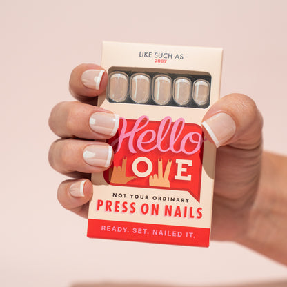 Hand holding a box of 'Hello Love' press-on nails with a pink background