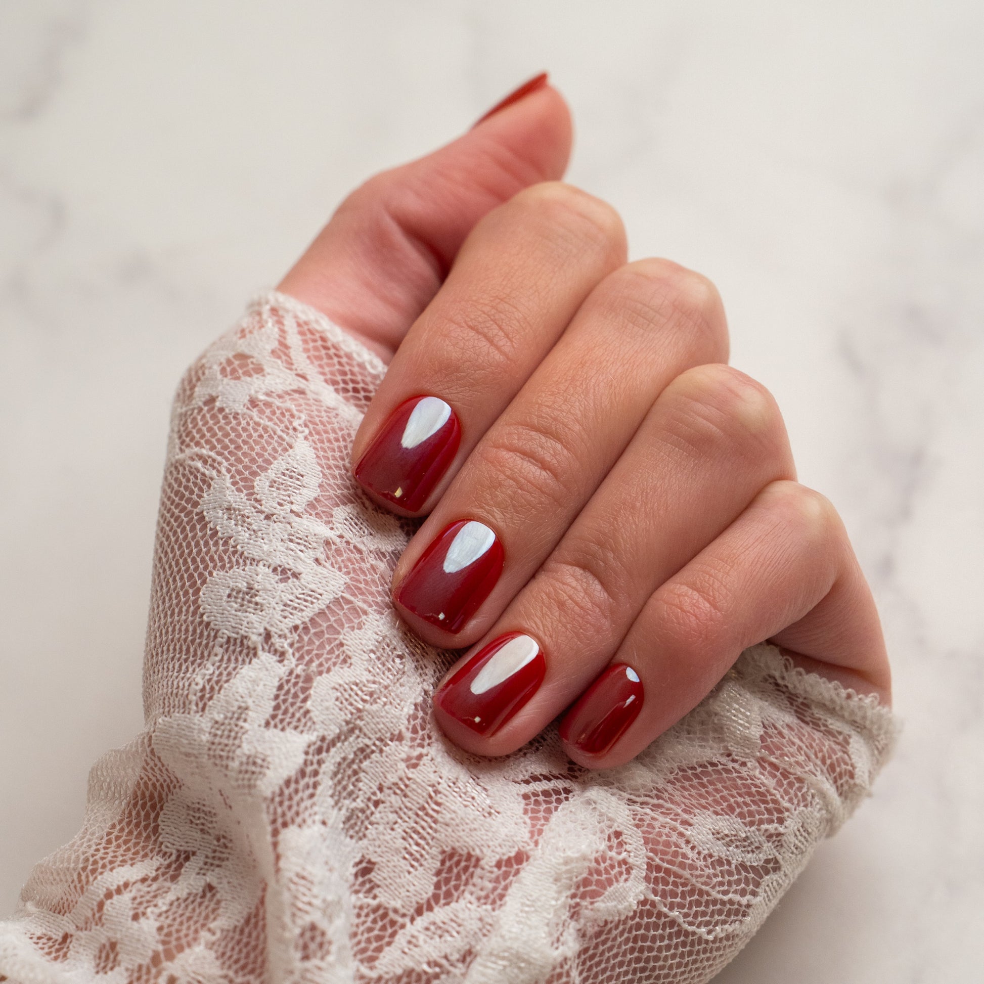Hand with red press on nails wearing a lace glove on a light background