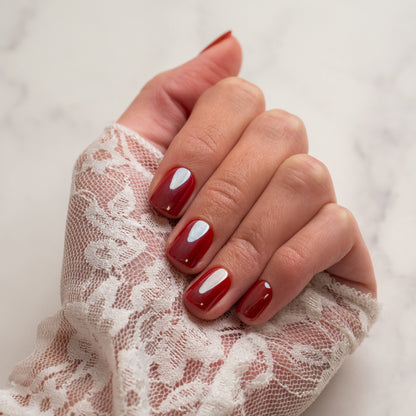 Hand with red press on nails wearing a lace glove on a light background